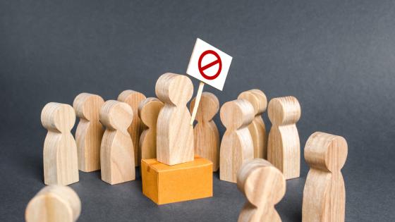 Wooden figures gather round one figure holding a no-entry flag